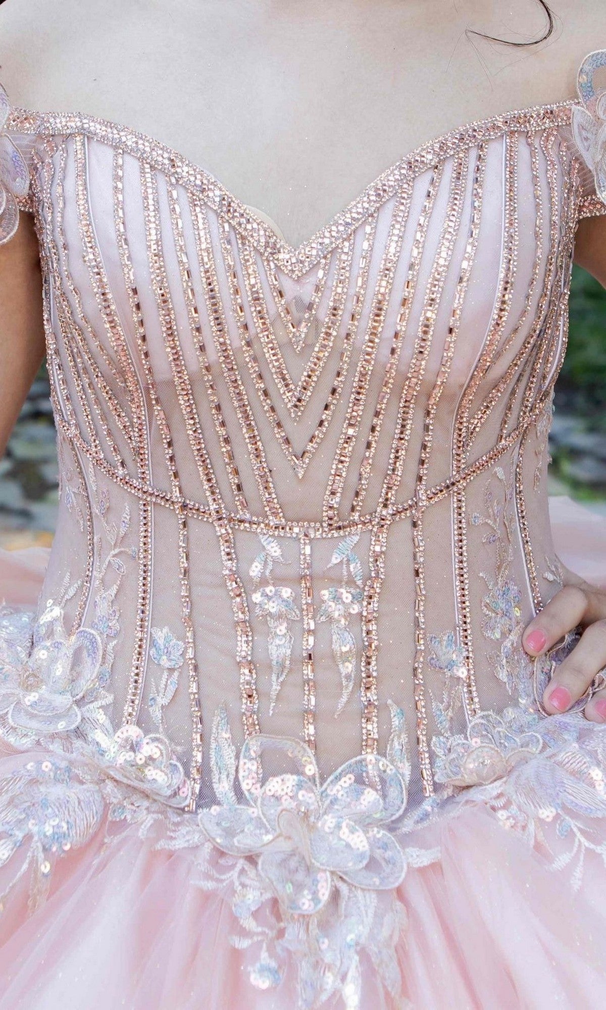 Close-up of a person wearing the Quinceanera Dress 8370J by Cinderella Couture—a pink, off-the-shoulder ball gown featuring beadwork, sequins, and floral appliques adorning its illusion corset bodice.